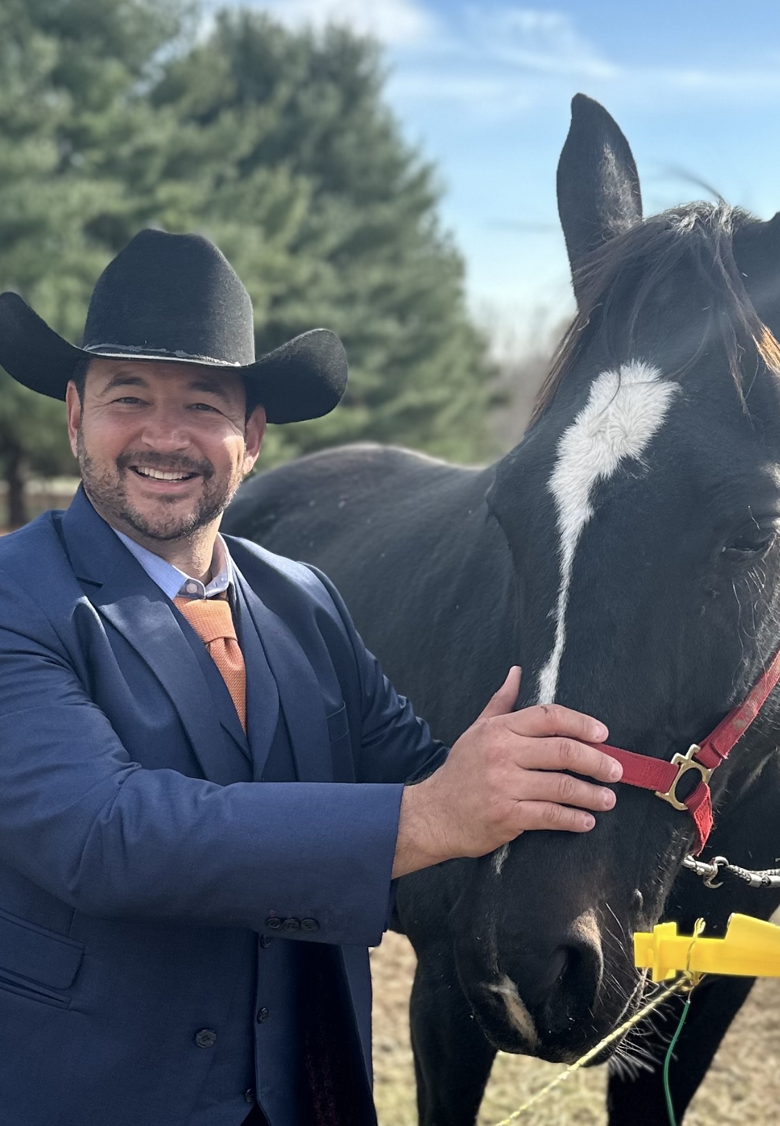 Founder in a cowboy hat and blue suit smiling next to a black rescue horse.